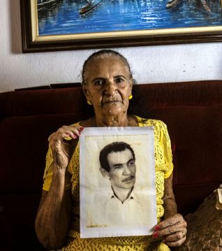 Foto da moradora segurando uma fotografia antiga do seu esposo.